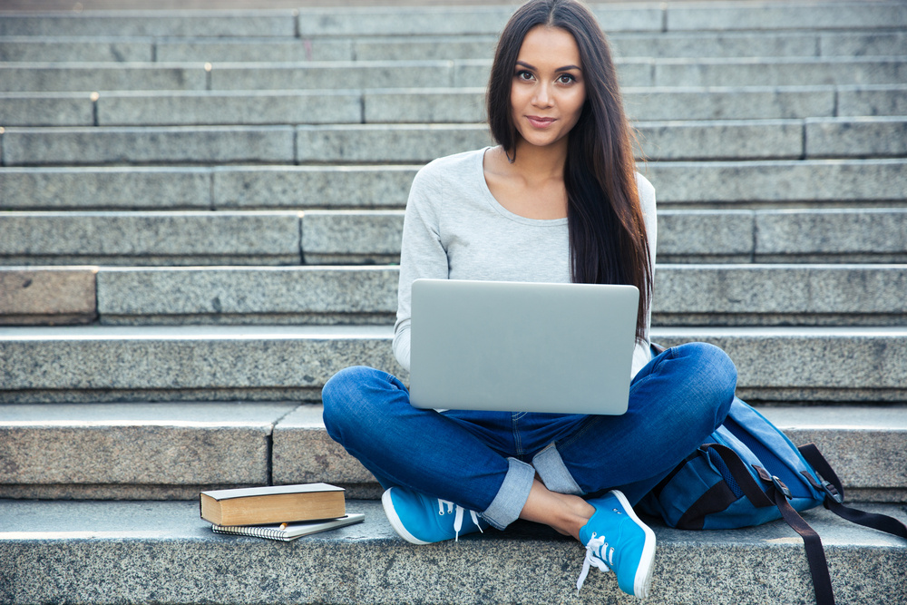 Portrait of a happy young woman sitting on the city stairs and using laptop computer outdoors Portrait of a happy young woman sitting on the city stairs and using laptop computer outdoors
